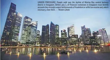  ??  ?? UNDER PRESSURE: People walk past the skyline of Marina Bay central business district in Singapore. Before July 1, all financial institutio­ns in Singapore must identify accounts they strongly suspect hold proceeds of fraudulent or wilful tax evasion...