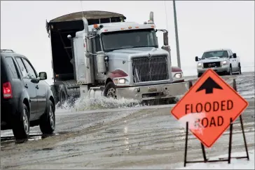  ?? @IMartensHe­rald Herald photos by Ian Martens ?? A sign warns motorists of flooding while a transport truck splashes through water over part of the intersecti­on of Highway 4 and Highway 845.