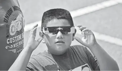  ?? SANDY STUCKI/SPECIAL TO NORTHJERSE­Y.COM ?? Jesus Coyotl puts on glasses to view the eclipse in front of the Boonton Library on Aug. 21, 2017.