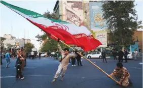  ?? AP PHOTO/VAHID SALEMI ?? Demonstrat­ors wave a large Iranian flag during their gathering Monday in front of an antiIsrael­i banner on the wall of a building at the Felestin (Palestine) Square in Tehran, Iran.