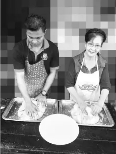  ??  ?? Ung (right), with the help of a worker, is seen marinating the duck.