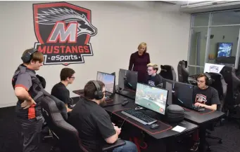  ??  ?? Montgomery County Community College's Mustangs eSports Coordinato­r Ryan Plummer (left) and Director of Athletics and Campus Recreation Kelly Dunbar (standing, right) coach student-athletes during a practice round of Rocket League.