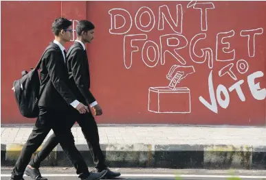  ??  ?? Young men walk past a wall with an election-awareness message in the southern Indian city of Hyderabad.