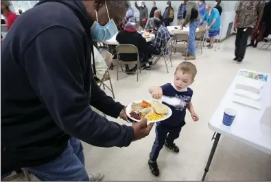  ?? (Arkansas Democrat-Gazette/Thomas Metthe) ?? Volunteer Calvin Ledbetter, 4, gives out silverware to diners Thursday during the Little Rock Compassion Center’s Thanksgivi­ng dinner in Little Rock.