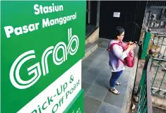  ??  ?? A woman uses her phone near a sign for the online ride-hailing service Grab at the Manggarai train station in Jakarta. Indonesia has set minimum and maximum tariffs for online car-hailing services, aiming to ensure comparable pricing with convention­al...