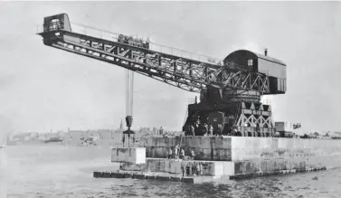  ??  ?? The same crane perhaps 20 years later with the work still ongoing. A civilian workforce of at least 18 men is on hand, their presence accentuati­ng the size of the Titan block-setting crane, its 115ft jib seen in the course of placing yet another block. On average, for the North Breakwater over 70ft depth of blockwork was being laid below sea level and the maximum width was 62ft, so it is hardly surprising that progress on the 1,500ft-long structure averaged about 40ft per year! A similar block sits on the railway wagon immediatel­y behind the crane – it must have seemed an endless job, especially given that the work was stopped during the two world wars.