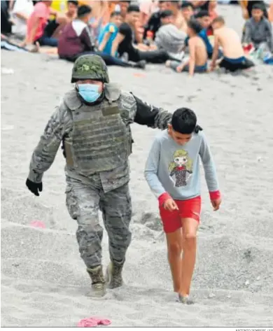  ?? ANTONIO SEMPERE / EP ?? Un militar del Ejército acompaña a un niño en una playa de Ceuta tras llegar a las costas de la ciudad.