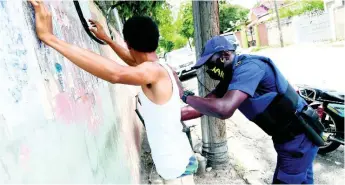  ??  ?? A member of the security forces searches a man along Arnold Road in Kingston yesterday.