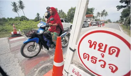  ?? PORNPROM SATRABHAYA ?? A motorist drives through a security checkpoint set up along a road in Pattani, where many roads in areas which are prone to unrest are under heavy surveillan­ce.