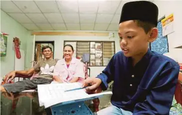  ?? PIC BY SHARUL HAFIZ ZAM ?? Mohammad Firdaus Hong Abdullah (right) reading ‘Iqra tiga’ at his home in Jitra yesterday. With him are his parents, Lim Hun Kheng (left), and Wandee Sandeesa.