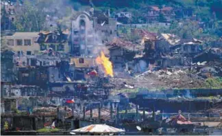  ?? REUTERSPIX ?? Flame rises from damaged buildings after government troops cleared an area in Marawi of insurgents yesterday.