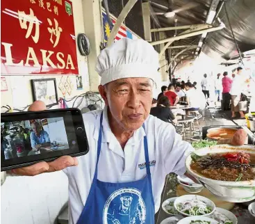  ??  ?? On record: Proprietor Kok Peoh showing a photograph of Bourdain eating at his stall in Ayer Itam with a bowl of assam laksa.