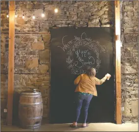  ??  ?? Stephanie Skoglund touches up paint on a giant chalkboard where guests can leave messages for the bride and groom at The Vault, the wedding and event center she owns in Tenino, Wash. The board still bears the names — Kyzer and Sandra — of the last couple to be married at the venue in March before the coronaviru­s outbreak forced them to close their doors. (AP/Ted S. Warren)