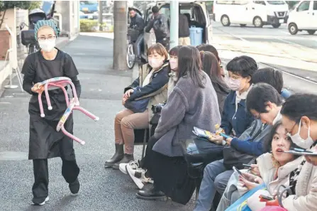  ?? ?? Ukon (left), who runs the restaurant Onigiri Bongo, a shop specialisi­ng in rice balls known as ‘onigiri’, giving out small stools for queueing customers to sit on over an hour before opening time, in the Otsuka area of Tokyo.