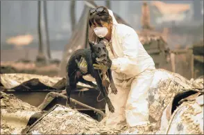  ?? AP PHOTO ?? A search-and-rescue worker looking for Camp Fire victims carries Susie Q. to safety after the cadaver dog fell through rubble at the Holly Hills Mobile Estates in Paradise, Calif.