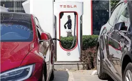  ?? [AP FILE PHOTO] ?? A security guard moves past an electric vehicle charging station in Beijing. Momentum is building worldwide for electric cars thanks to rising government fuel economy standards and climate concerns. Automakers are jumping on board. But selling those...