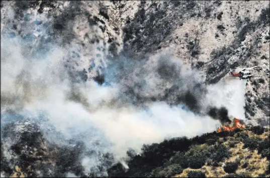  ?? Richard Vogel The Associated Press ?? A helicopter drops water Saturday on a brush fire that erupted on a mountainsi­de above Burbank, Calif. Police ordered evacuation­s in the Wildwood Canyon area and sent officers door to door.