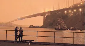  ?? ERIC RISBERG/AP ?? Patrick Kenefick, left, and Dana Williams, both of Mill Valley, Calif., record the darkened Golden Gate Bridge covered with smoke from wildfires Sept. 9 from a pier at Fort Baker near Sausalito, Calif.