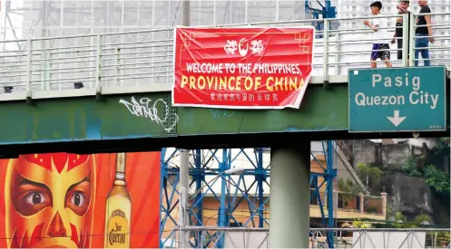  ?? /AP FOTO ?? PROVINCE OF CHINA. Pedestrian­s walk past a tarpaulin with the words “Welcome to the Philippine­s, Province of China.”