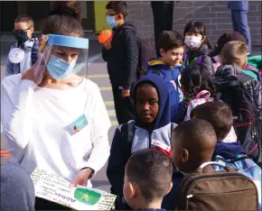  ?? The Canadian Press ?? A teacher wearing protective equipment greets her students in the school yard at the PhilippeLa­barre Elementary School in Montreal, on Thursday. Thousands of Quebec students return to class in the shadow of the COVID-19 pandemic.