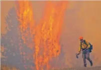  ?? PETE CASTER/ASSOCIATED PRESS ?? After walking down a gravel road to do recon on a fire cresting into the trees, a wildland firefighte­r grimaces Thursday as he walks back to his crew at the Bedrock Fire north of Lenore, Idaho. Winds and low humidity have caused extreme fires.