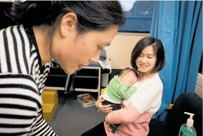  ?? Photo / Dean Purcell ?? Huie Chen holds her baby Bryan Wang as public health nurse Alice Ma prepares the TB vaccine.