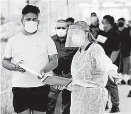  ?? MARCIO JOSE SANCHEZ/AP ?? Residents line up behind a health care worker Wednesday at a testing site in Los Angeles. California’s confirmed infections have surpassed New York for the most in the country.