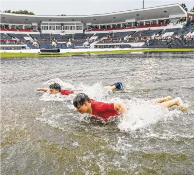  ?? THE ASSOCIATED PRESS ?? Park crew members Jack Burkes, foreground, and Cole Catalano swim in the water in the outfield following heavy rainfall at Oxford-University Stadium during a delay in their Oxford Regional game Friday in Oxford, Miss.