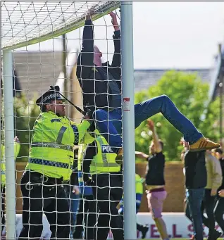  ??  ?? Climbing frame: An officer with a baton tackles a fan hanging from the goalposts