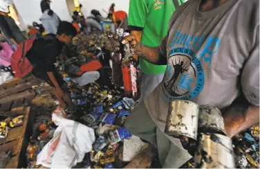  ?? Dita Alangkara / Associated Press ?? A man holds bottles of syrup and cans of milk scavenged from an abandoned warehouse in Palu.