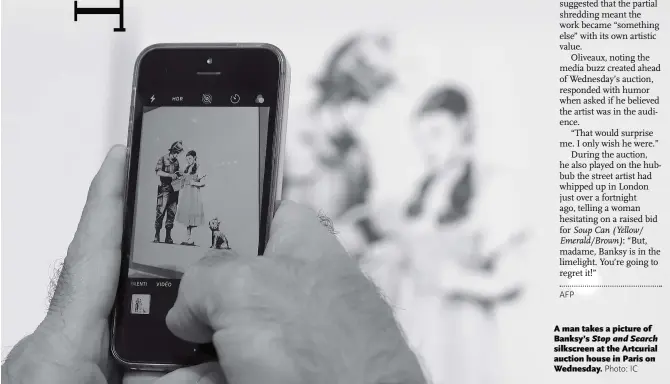  ?? Photo: IC ?? A man takes a picture of Banksy’s Stop and Search silkscreen at the Artcurial auction house in Paris on Wednesday.