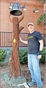  ?? Contribute­d ?? Metal artist Mark Baker stands beside the old Williams farm bell and its new “tree” post, which he crafted and recently installed in the Joanne Owens Sculpture Garden in front of the Harris Arts Center, downtown Calhoun.