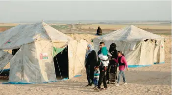  ?? — AFP ?? A family walks past tents pitched by Palestinia­ns on the Gaza border with Israel, east of Jabalia, on Thursday.