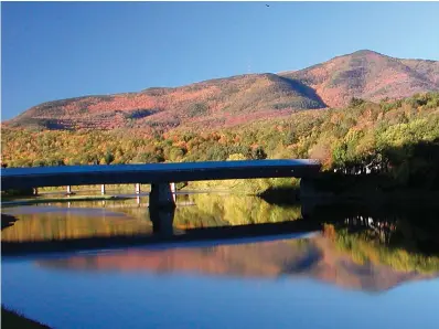  ?? AP Photo/Barbara Noll, File ?? A covered bridge, center, that runs between Cornish, N.H., and Windsor, Vt., is reflected in the Connecticu­t River along with Mount Ascutney, top right, on Oct. 14, 2002, in a view from the Cornish side of the river. When the Ascutney ski resort closed in 2010 because of scant snow and mismanagem­ent, it threatened to take with it the nearby community of West Windsor, Vt., population 1,099.