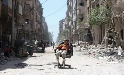  ?? (Ali Hashisho/Reuters) ?? A BOY SITS on a damaged street in Douma in Damascus on Monday.