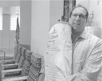  ?? TERRY SPENCER, ASSOCIATED PRESS ?? Rabbi Adam Miller of Temple Shalom in Naples, Florida, holds the Torah he took to Tennessee to protect it from hurricane Irma. Miller has rewritten his Rosh Hashanah sermon to reflect the damage done to southwest Florida by the storm.