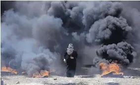  ?? KHALIL HAMRA/ASSOCIATED PRESS ?? A Palestinia­n woman walks through black smoke from burning tires on the Gaza Strip’s border with Israel on Monday. At least 58 protesters were killed during the violence.