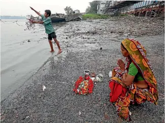  ??  ?? A woman offers prayers as a boy searches for coins with a piece of magnet, on the banks of river Ganges, in Kolkata.