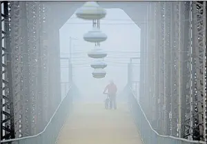  ?? Arkansas Democrat-Gazette/STATON BREIDENTHA­L ?? Fredrick Williams Jr. walks across the Clinton Presidenti­al Center Bridge on Wednesday afternoon as fog shrouds the Arkansas River.