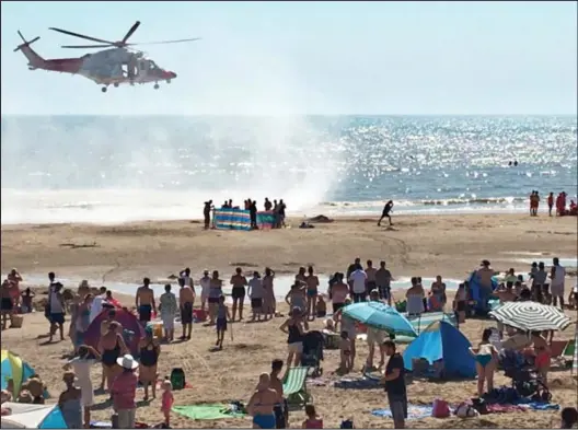  ??  ?? Tragedy on the sand: Beachgoers, who were warned not go into the water, watch as a Coastguard helicopter helps in the search