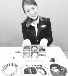  ??  ?? A JAL cabin attendant shows Japanese in-flight meals supervised by Chef Jun Kurogi, at the JAL Royal Catering Co. Haneda facility in Tokyo on Friday.