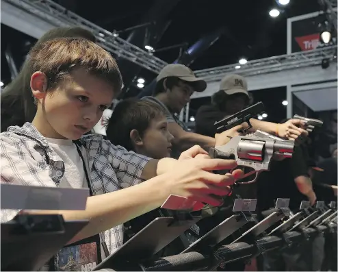  ?? JUSTIN SULLIVAN / GETTY IMAGES ?? Children try out guns at a National Rifle Associatio­n annual meeting. The America of the NRA’s imaginatio­n is a mythic, death-match arena populated by “good guys” and “bad guys,” “monsters” and “patriots,” Jonathan Kay says.