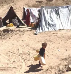  ??  ?? A child carries water jugs at a camp. Some 120,000 people have sought refuge outside Qala-e Nau in recent months.