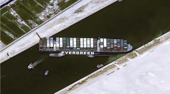  ?? GETTY IMAGES PHOTOS ?? RUN AGROUND: A container ship is stuck sideways in the Suez Canal, blocking the shipping lane and disrupting world distributi­on of products. Workers are using backhoes, dredging machines and tugboats to try to spring it free.