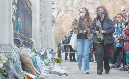  ?? Alastair Grant The Associated Press ?? Two people carry flowers Friday to place by the gate at Buckingham Palace in London to honor Prince Philip, who died at 99.