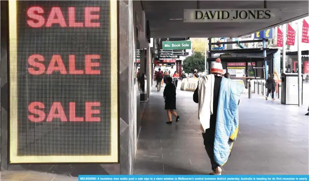  ?? AFP ?? MELBOURNE: A homeless man walks past a sale sign in a store window in Melbourne’s central business district yesterday. Australia is heading for its first recession in nearly three decades after the economy shrunk in the January-March quarter.—