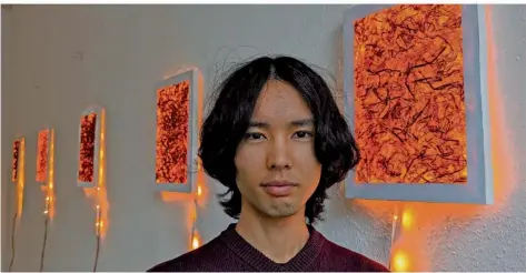  ?? FOTO: SILVIA BUSS ?? Der japanische Künstler Kazuki Taguchi vor den orange-leuchtende­n Rahmen seiner Installati­on. Orange gilt in Japan laut dem Künstler als die Farbe der Dämmerung, der Zeit zwischen Tag und Nacht. Eine Zeit, die Japanern nicht geheuer ist: „Man sagt bei uns dann, das Monster kommt.“
