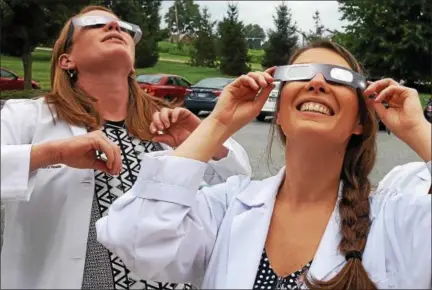  ?? BARRY TAGLIEBER — FOR DIGITAL FIRST MEDIA ?? Denisse DeCecco , right, a graduate student from Drexel University, watches the solar eclipse Monday afternoon outside her work at Main Line Health Care in Collegevil­le. She was one of millions of Americans who looked to the skies at this historic event.