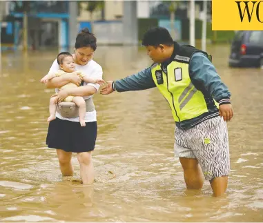  ?? NOEL CELIS / AFP VIA GETTY IMAGES ?? People wade down a flooded street following a heavy rain on Thursday in Zhengzhou, in China's Henan province.