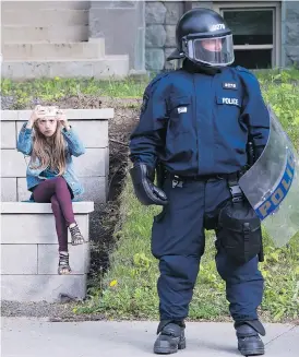  ?? PAUL CHIASSON / THE CANADIAN PRESS ?? A young girl takes a photo on her cellphone beside a police officer in riot gear as he stands watch ahead of a planned G7 protest in Quebec City on Thursday.